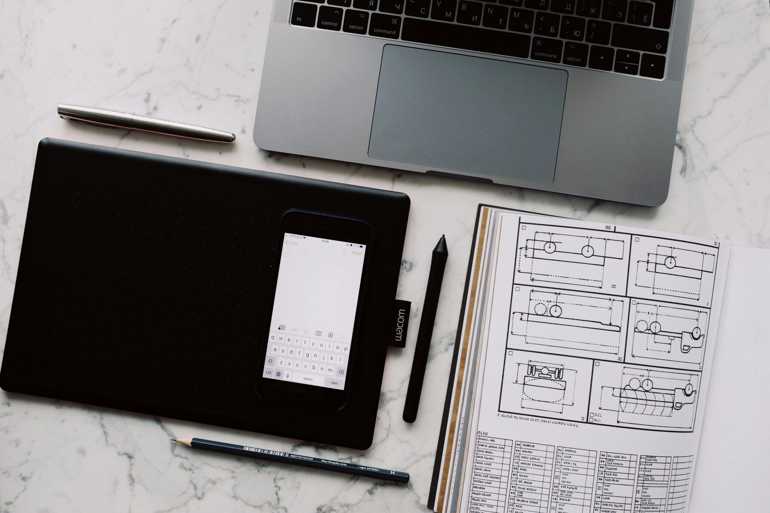 Top view of a creative workspace with a laptop, graphic tablet, and sketches.